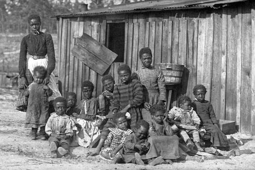 African American woman and twelve children stand outside a shed (1)